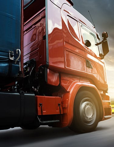 Camion de livraison rouge roulant vite : transport logistique Tracteur routier rouge vif en mouvement rapide, gros plan sur la cabine et la roue avant, lumière du soleil.